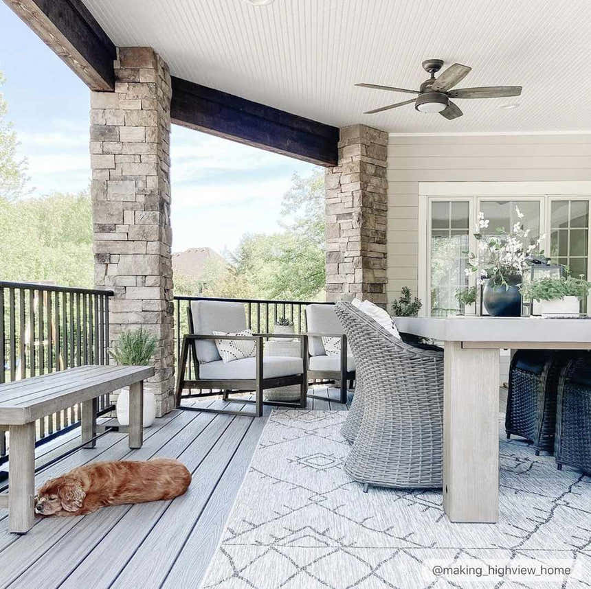 Outdoor patio scene with a Marwood Nordic Performance Rug, gray furniture, stone pillars, and a sleeping dog. Styleshot