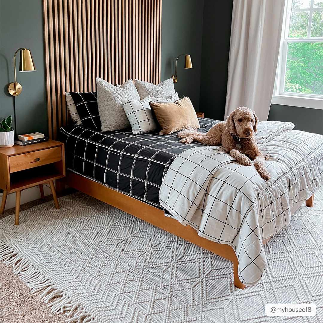 Bedroom scene with ivory Ramsbury Wool Area Rug, wood bed frame, black and white bedding, and a cute dog. Roomscene-Rectangle