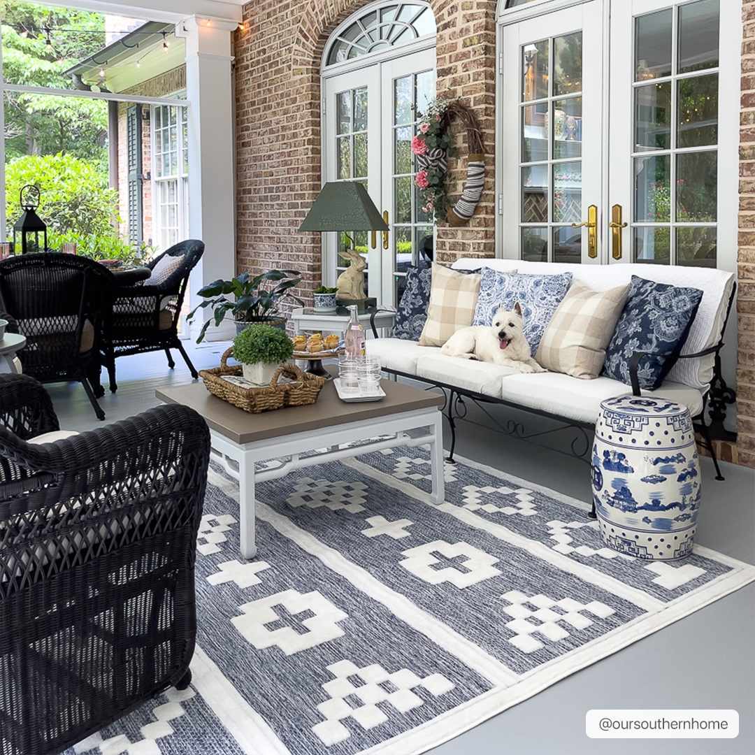 Covered porch with brick wall, white sofa, and Hiro Blue Outdoor Rug. Dog lounging on the sofa. Roomscene-Rectangle