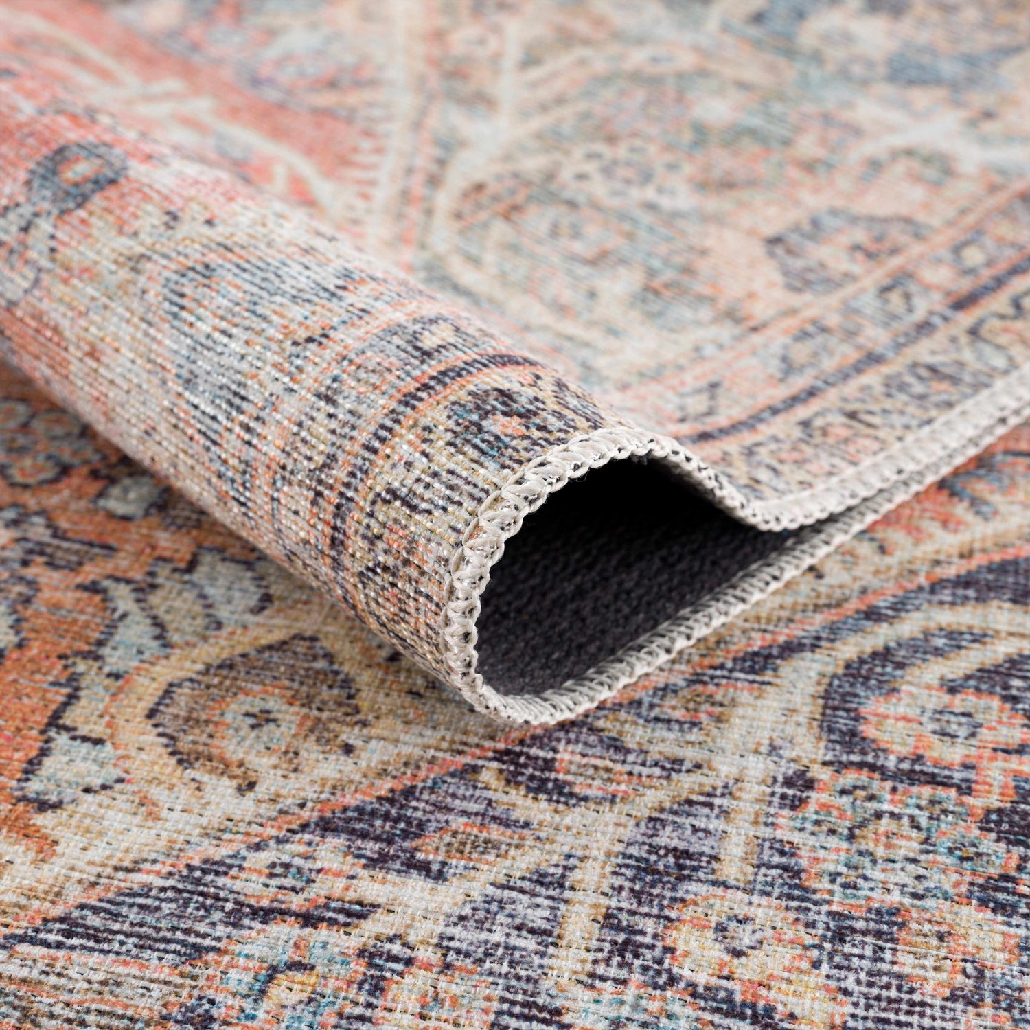 Close-up of rolled Konstantina Washable Area Rug showing Persian-style design in aqua, beige, brown, and dark blue. Fold