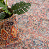 Close-up of the Urpi Rose & Blue Washable Area Rug featuring a traditional Persian pattern and a plant in a basket. Styleshot