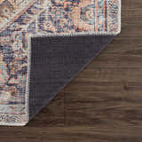 Close-up of Konstantina Washable Area Rug showing aqua, beige, and brown Persian-style pattern and non-slip backing on wood floor. Fold