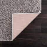 Close-up of the Judy Solid Gray Washable Shag Rug showing its soft texture and non-slip backing on dark wood floor. Back