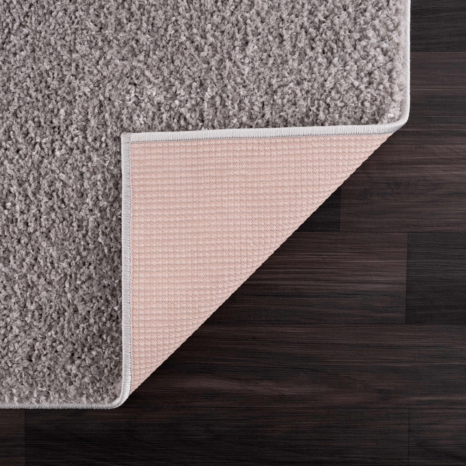 Close-up of the Judy Solid Gray Washable Shag Rug showing its soft texture and non-slip backing on dark wood floor. Back