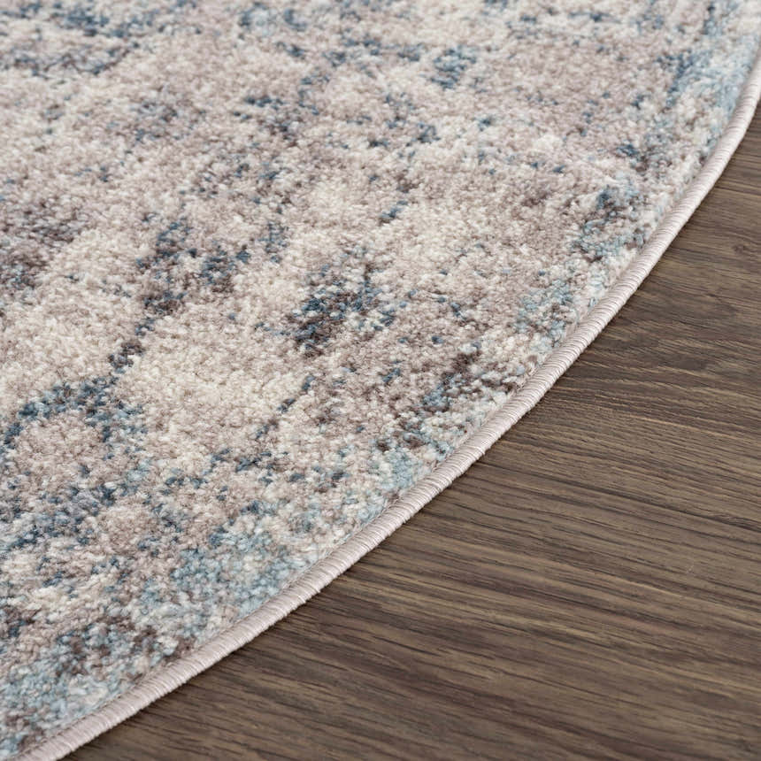 Close-up of the Orrick Area Rug showing its blue, cream, and brown tones, plus soft texture and machine-woven construction. Corner