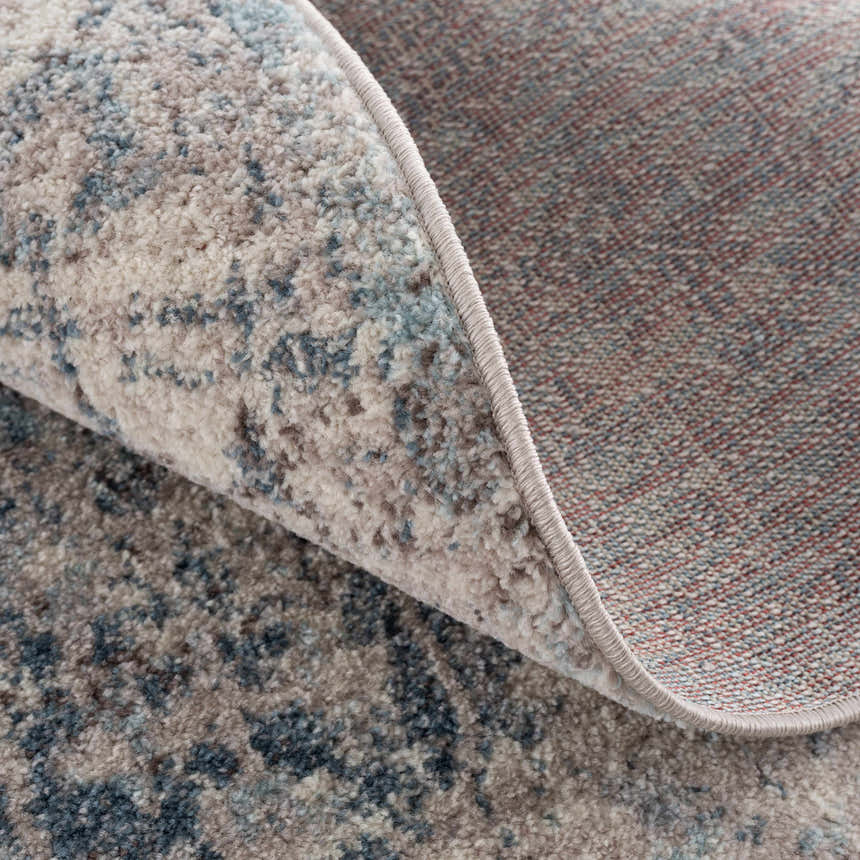 Close-up of the Orrick Area Rug showing the blue, cream, and brown abstract pattern and woven texture. Fold