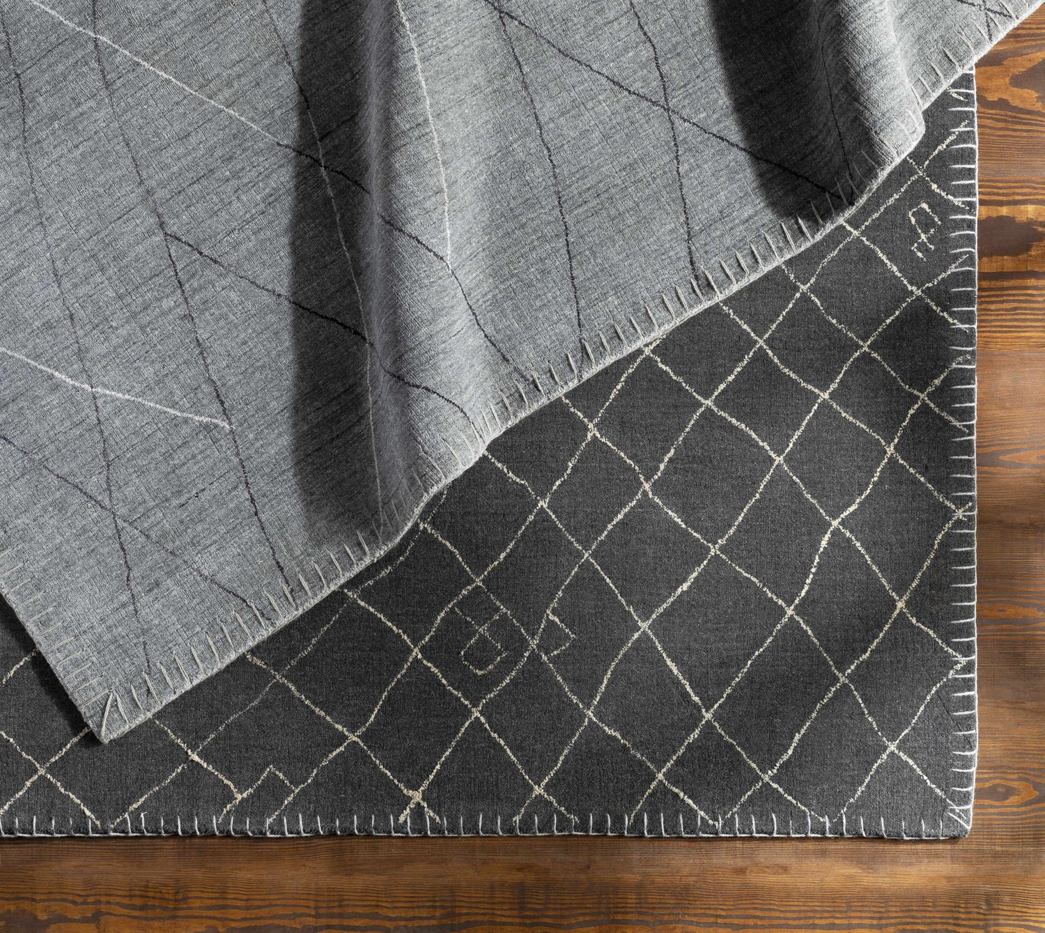 Close-up of the Brimbank Premium Rug. Black wool rug with ivory geometric diamond pattern and hand-loomed fringe detail. Styleshot