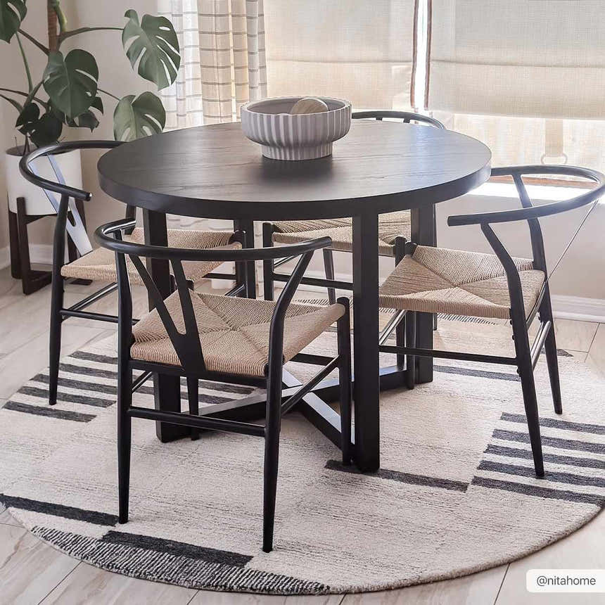 Dining room featuring a round, black table and chairs on the beige Aibonito Hand Tufted Wool Area Rug. Roomscene-Round
