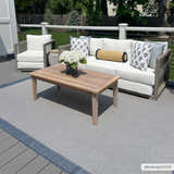 Outdoor patio scene with the Aleid Blue Area Rug, a wood coffee table, and wicker seating with white cushions. Roomscene-Rectangle