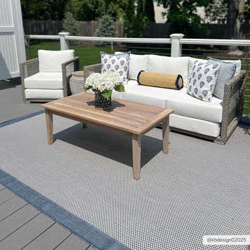 Outdoor patio scene with the Aleid Blue Area Rug, a wood coffee table, and wicker seating with white cushions. Roomscene-Rectangle