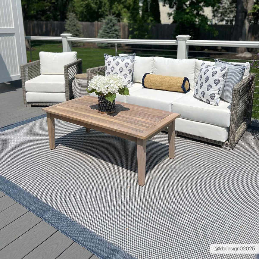 Outdoor patio scene with the Aleid Blue Area Rug, a wood coffee table, and wicker seating with white cushions. Roomscene-Rectangle