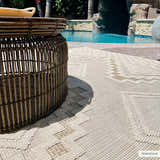 Outdoor patio scene with a round Arwid Bone Area Rug under a wicker table near a pool. Styleshot