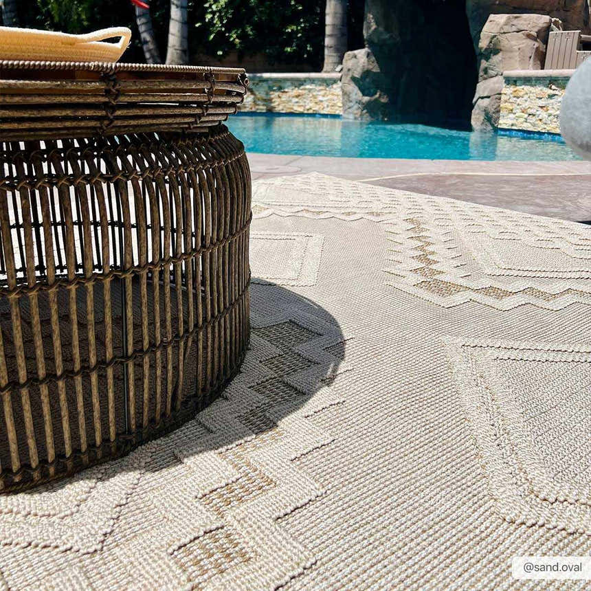 Outdoor patio scene with a round Arwid Bone Area Rug under a wicker table near a pool. Styleshot