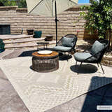 Outdoor patio scene with Arwid Bone Area Rug, wicker furniture, and neutral tones under a sun umbrella. Roomscene-Rectangle