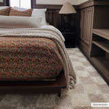 Bedroom scene with a light brown Atira Checkered Area Rug, dark wood furniture, and a patterned bedspread. Roomscene-Rectangle