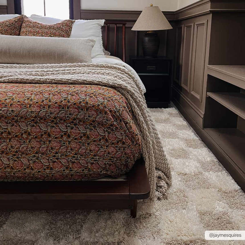 Bedroom scene with a light brown Atira Checkered Area Rug, dark wood furniture, and a patterned bedspread. Roomscene-Rectangle