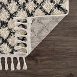 Close-up of the Muni Berber Shag Rug showing charcoal and light beige pattern, tassels, and machine-woven construction. Fold