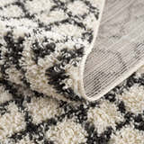 Close-up of the Muni Berber Shag Rug showing its charcoal and light beige colors, shag texture, and woven backing. Fold