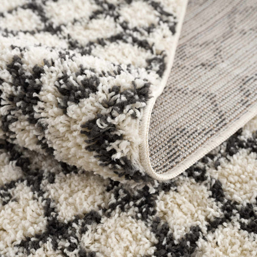 Close-up of the Muni Berber Shag Rug showing its charcoal and light beige colors, shag texture, and woven backing. Fold