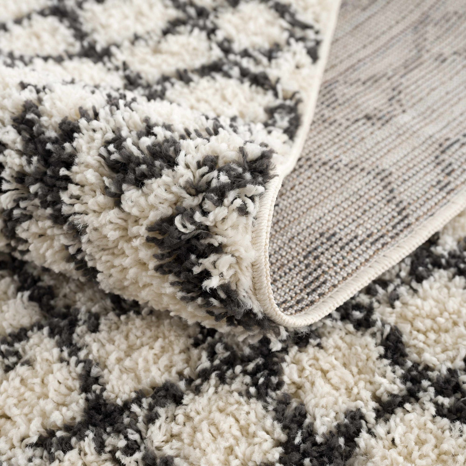Close-up of the Muni Berber Shag Rug showing its charcoal and light beige colors, shag texture, and woven backing. Fold