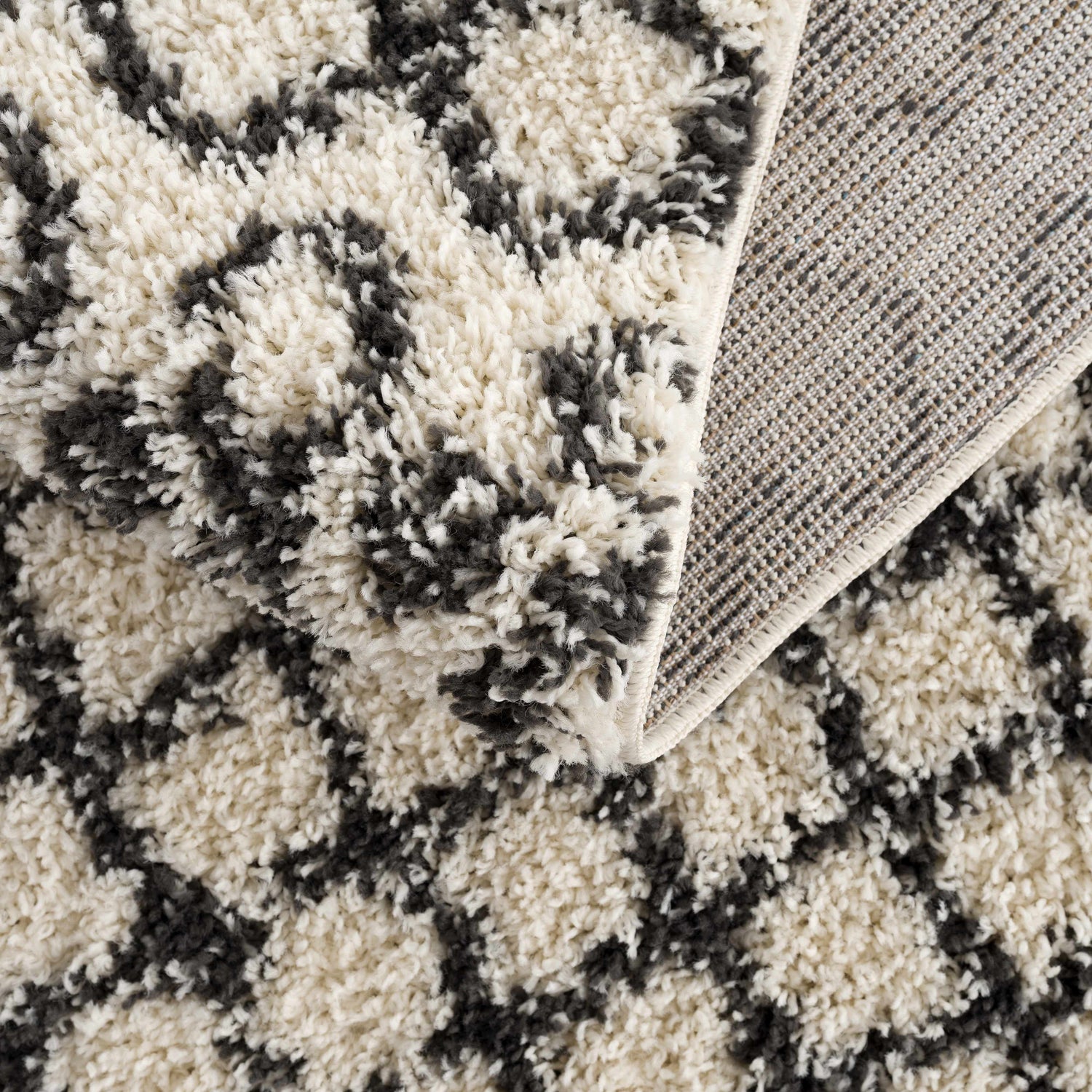 Close-up of the Muni Berber Shag Rug showing charcoal and light beige colors and shag texture. Machine woven construction detail. Fold