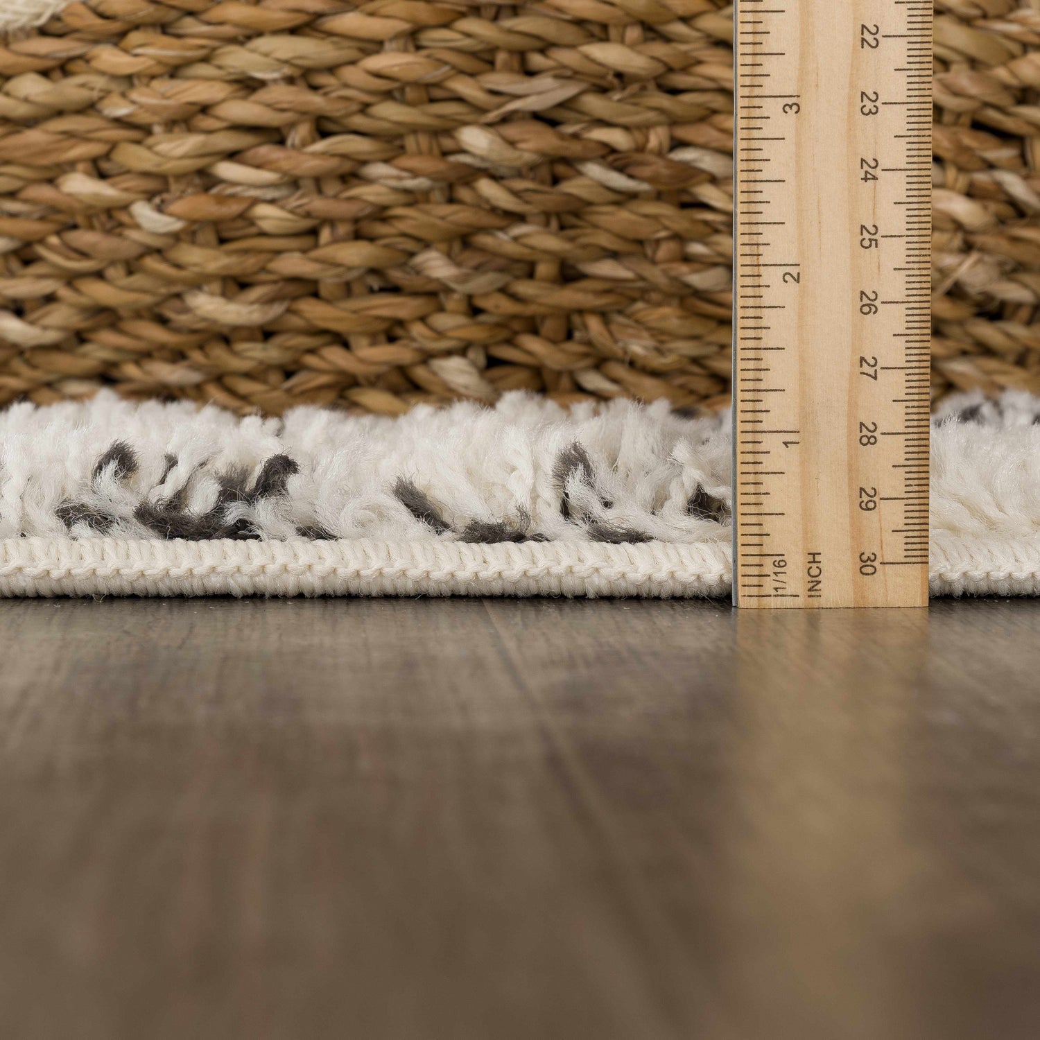 Close-up of Kibureau Area Rug shag pile, beige and charcoal colors, with a ruler showing pile height. Styleshot
