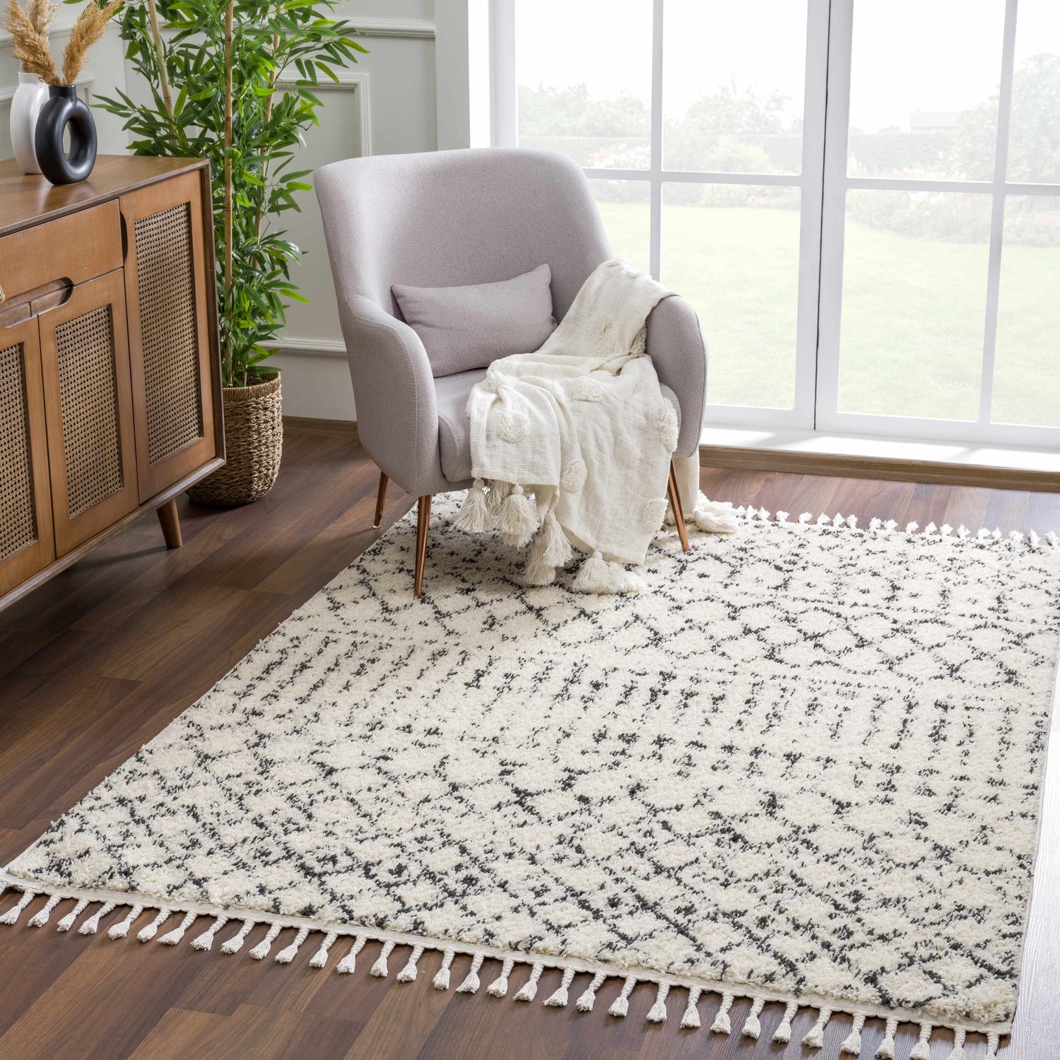 Living room scene with a beige and charcoal Kibureau Area Rug, gray chair, and wood cabinet. Roomscene-Rectangle