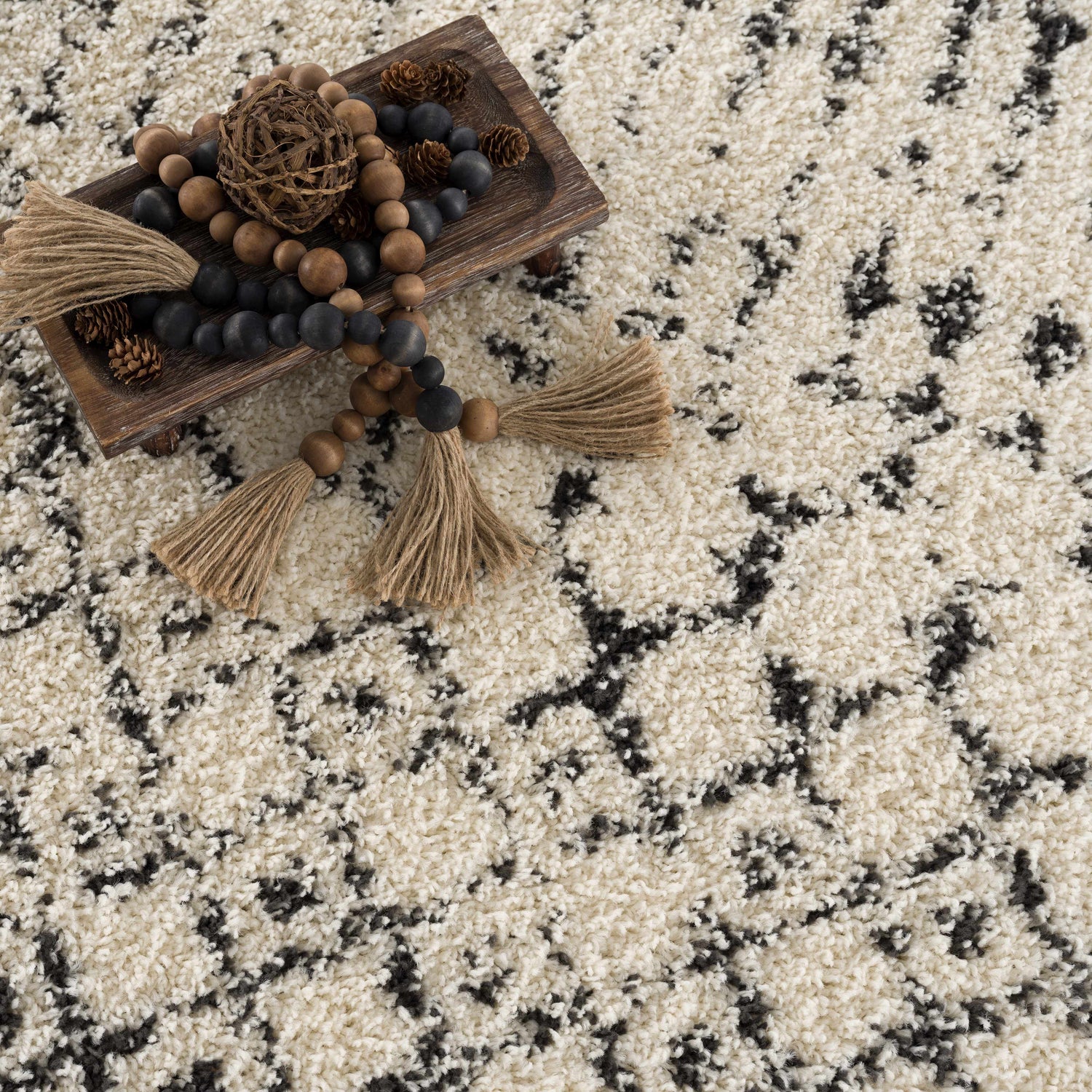 Close-up of the Kibureau Area Rug. Beige shag rug with charcoal Moroccan-inspired pattern and decorative wood beads. Texture