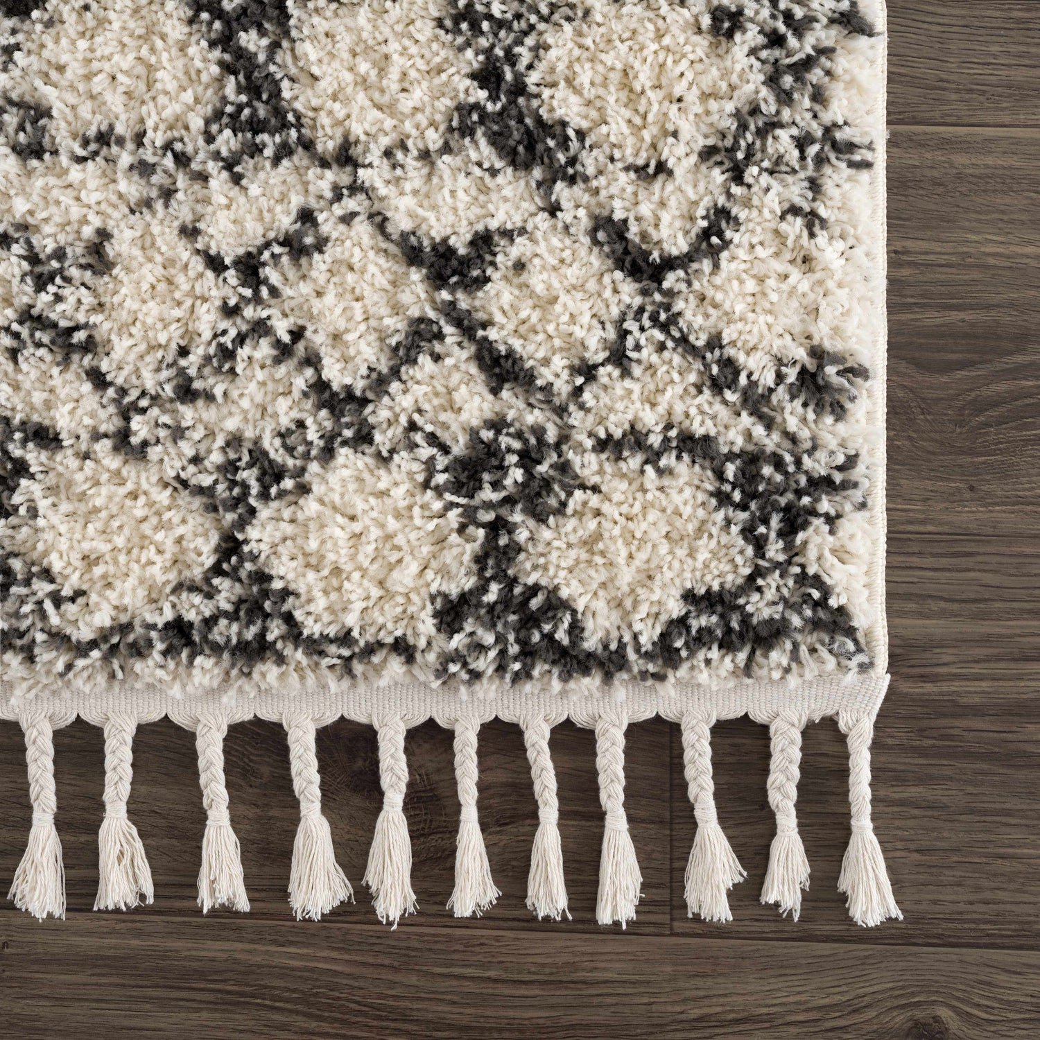 Close-up of the Buan Area Rug. Charcoal and light gray shag rug with tassels on a dark wood floor. Moroccan style. Swatch