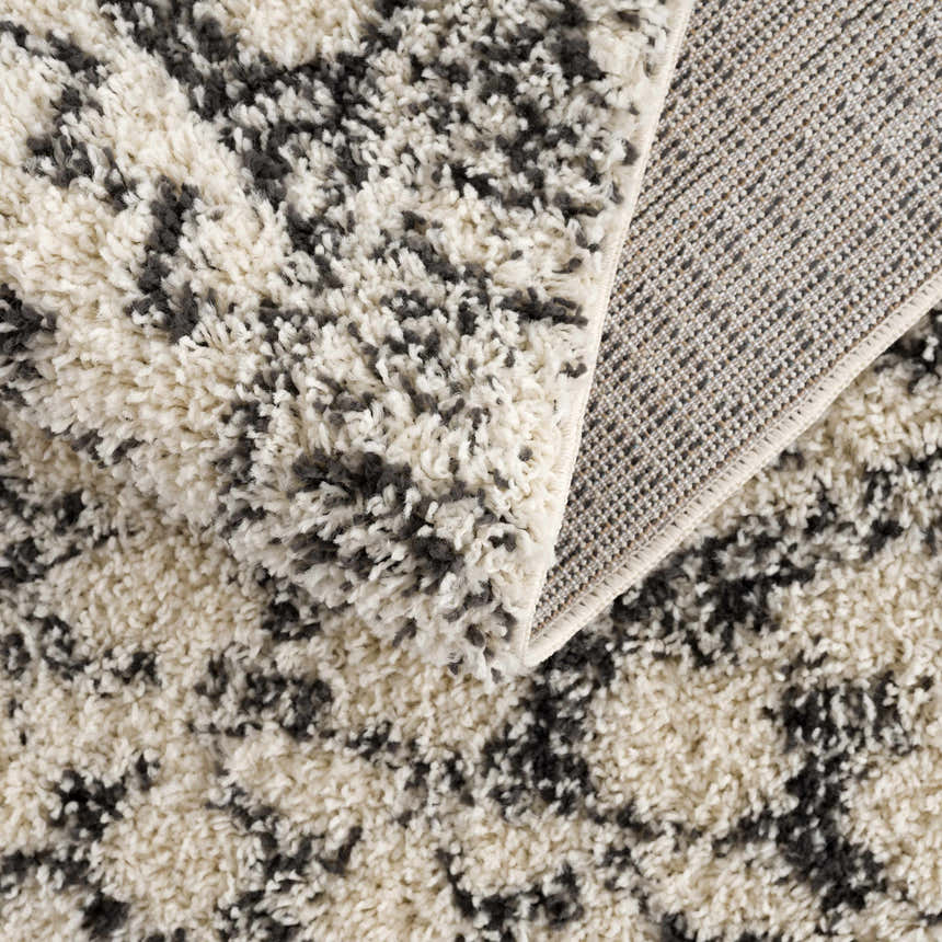Close-up of the Buan Area Rug showing its shag texture, charcoal and light gray pattern, and machine-woven backing. Fold