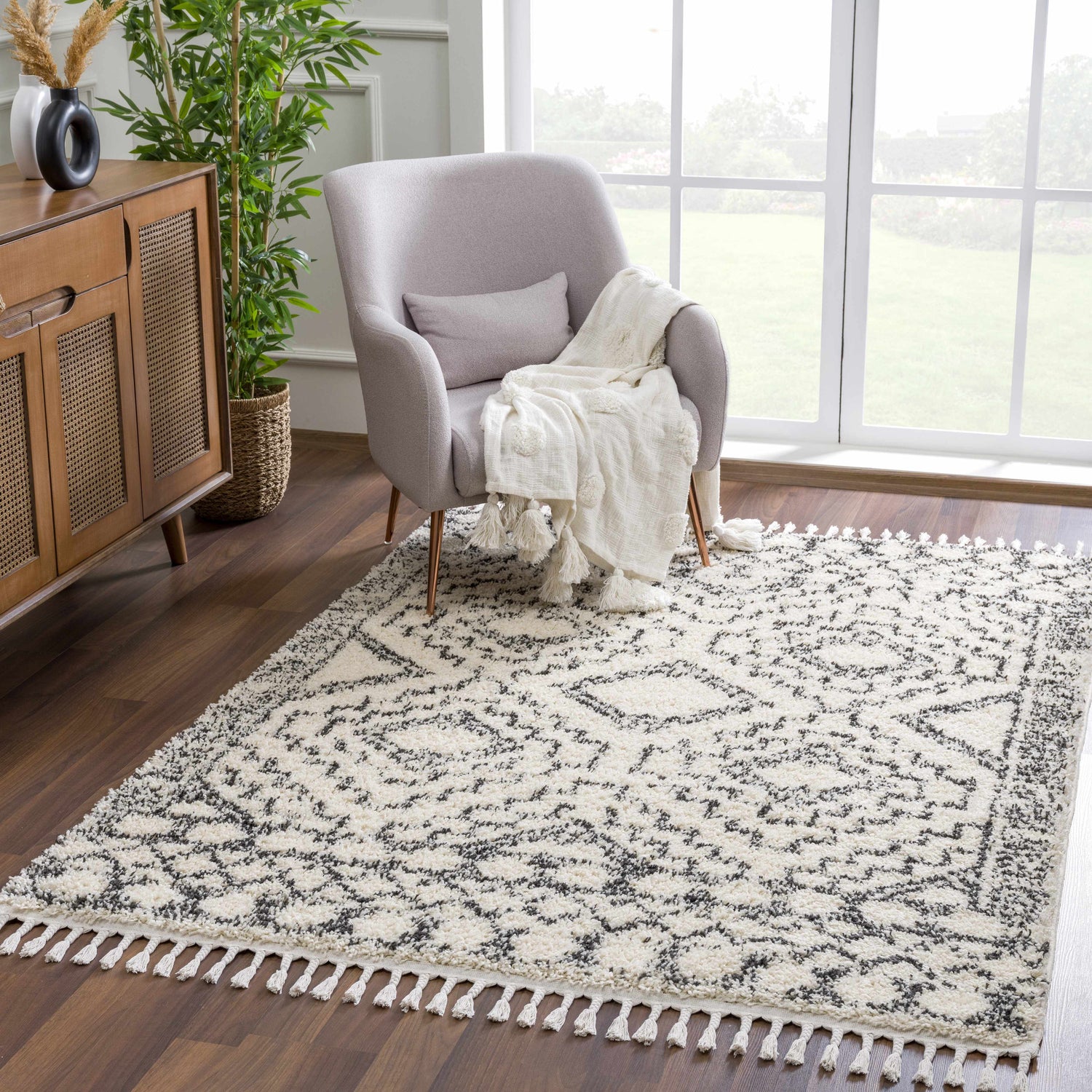 Living room scene with gray chair and Buan Area Rug in charcoal, dark gray, and light gray with a Moroccan-inspired design and tassel fringe. Roomscene-Rectangle