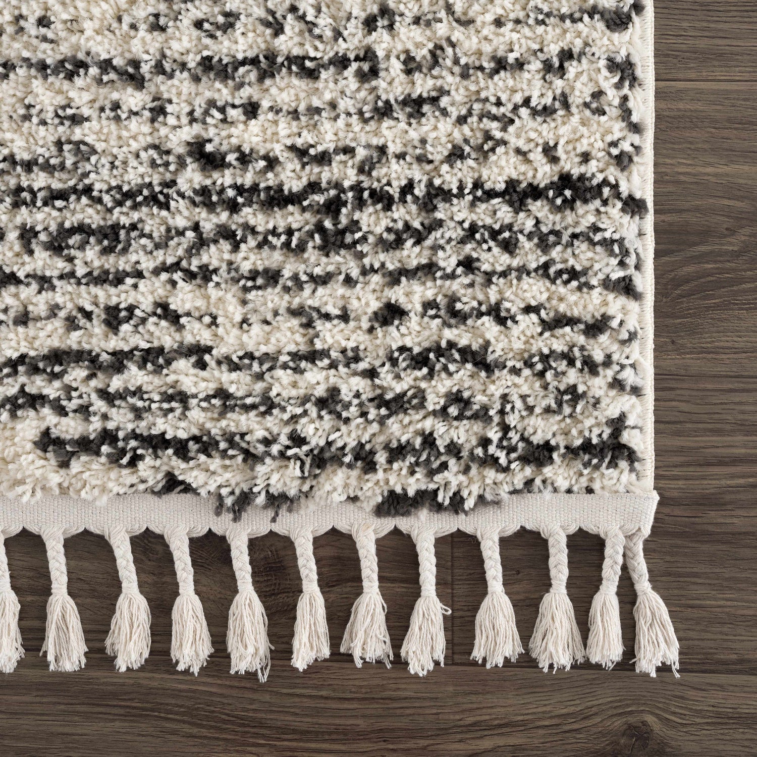 Close-up of the Howth Area Rug showing its bone and dark gray shag texture and decorative tassels. Swatch