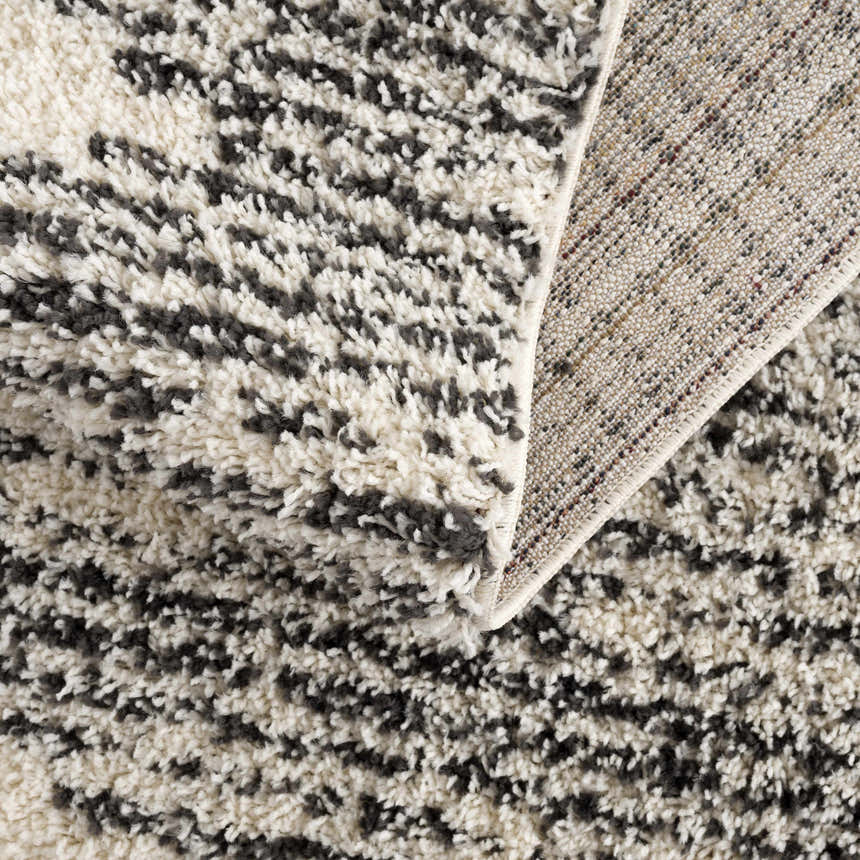 Close-up of the shag Howth Area Rug. Bone and dark gray Moroccan design, machine woven texture, and polypropylene material. Fold