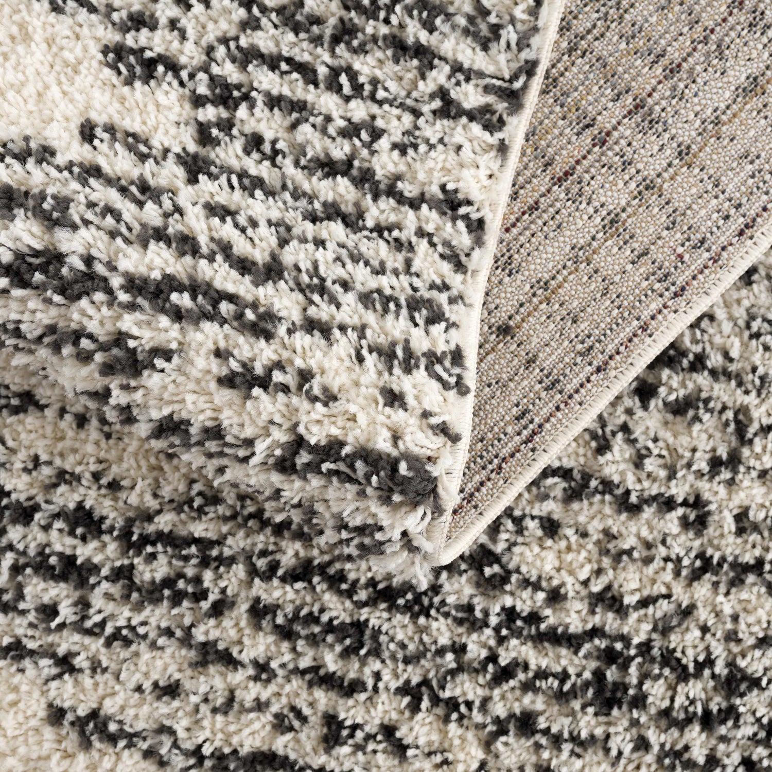 Close-up of the shag Howth Area Rug. Bone and dark gray Moroccan design, machine woven texture, and polypropylene material. Fold