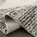 Close-up of the Howth Area Rug showcasing its bone and dark gray shag texture and machine-woven construction. Fold