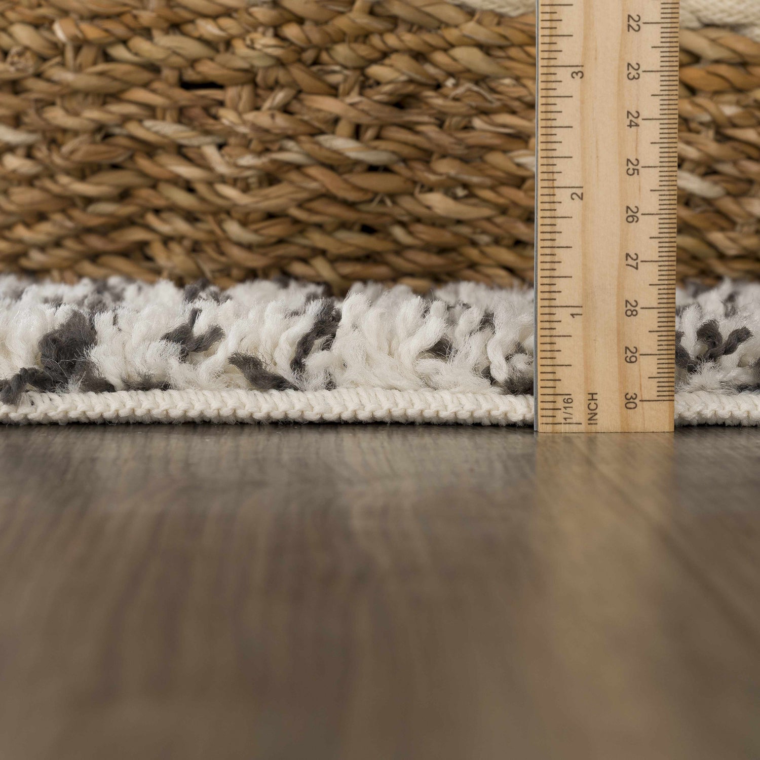 Close-up of the bone and dark gray Howth Area Rug showing its shag texture and height with a ruler. Pile