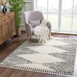 Living room scene with a bone and dark gray Howth Area Rug, gray chair, and wood cabinet. Roomscene-Rectangle