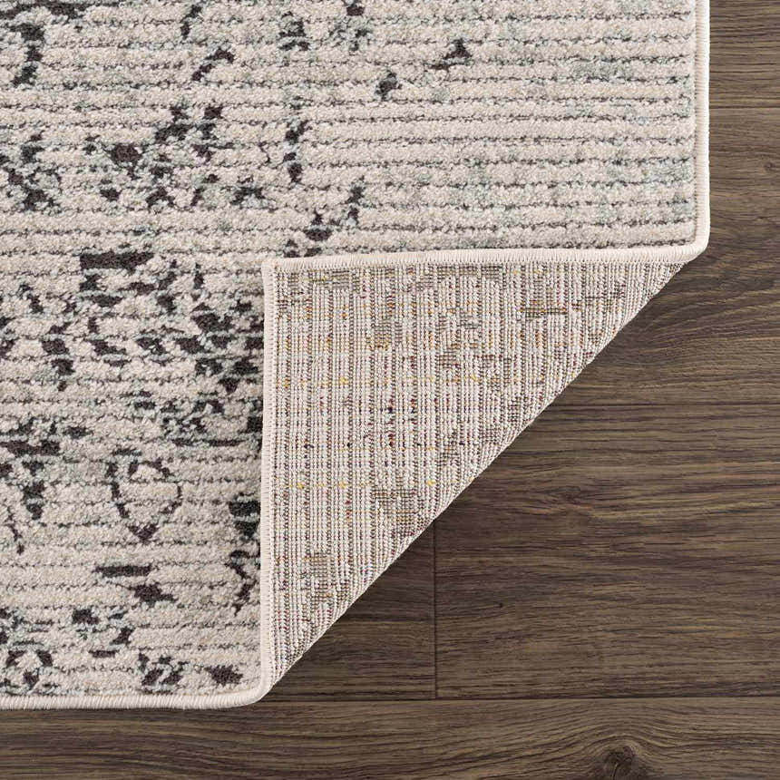 Close-up of Paicines Area Rug showing charcoal, gray, and beige traditional pattern and machine woven construction. Fold