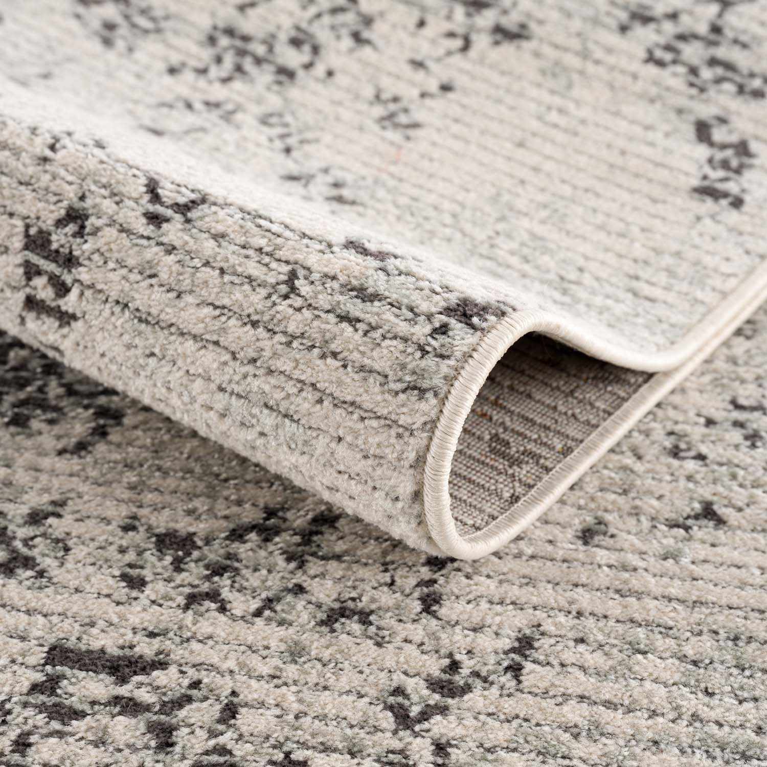 Close-up of the Paicines Area Rug showing its charcoal, gray, and light beige traditional pattern and machine-woven texture. Fold