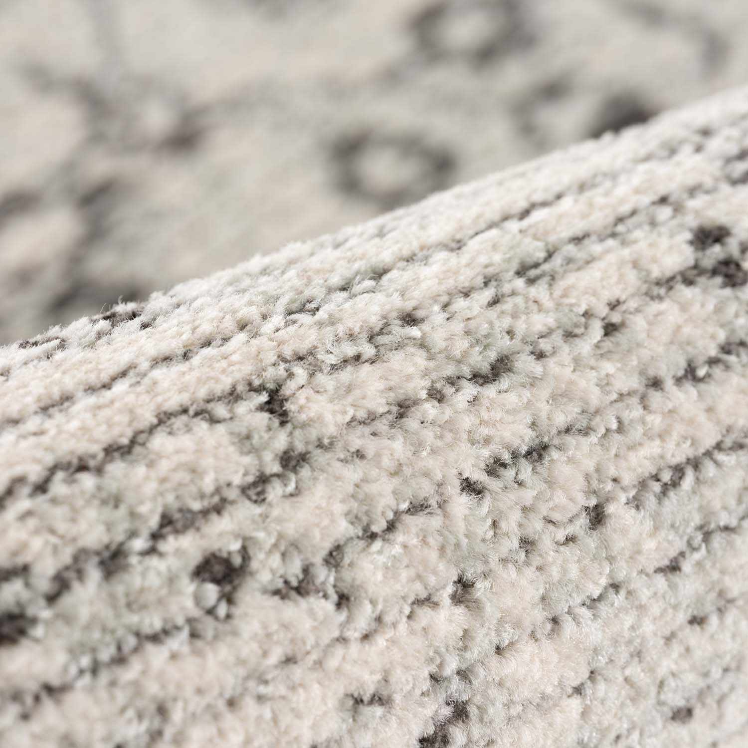 Close-up of the Paicines Area Rug showing its light beige, gray and charcoal traditional pattern and soft, textured pile. Fold
