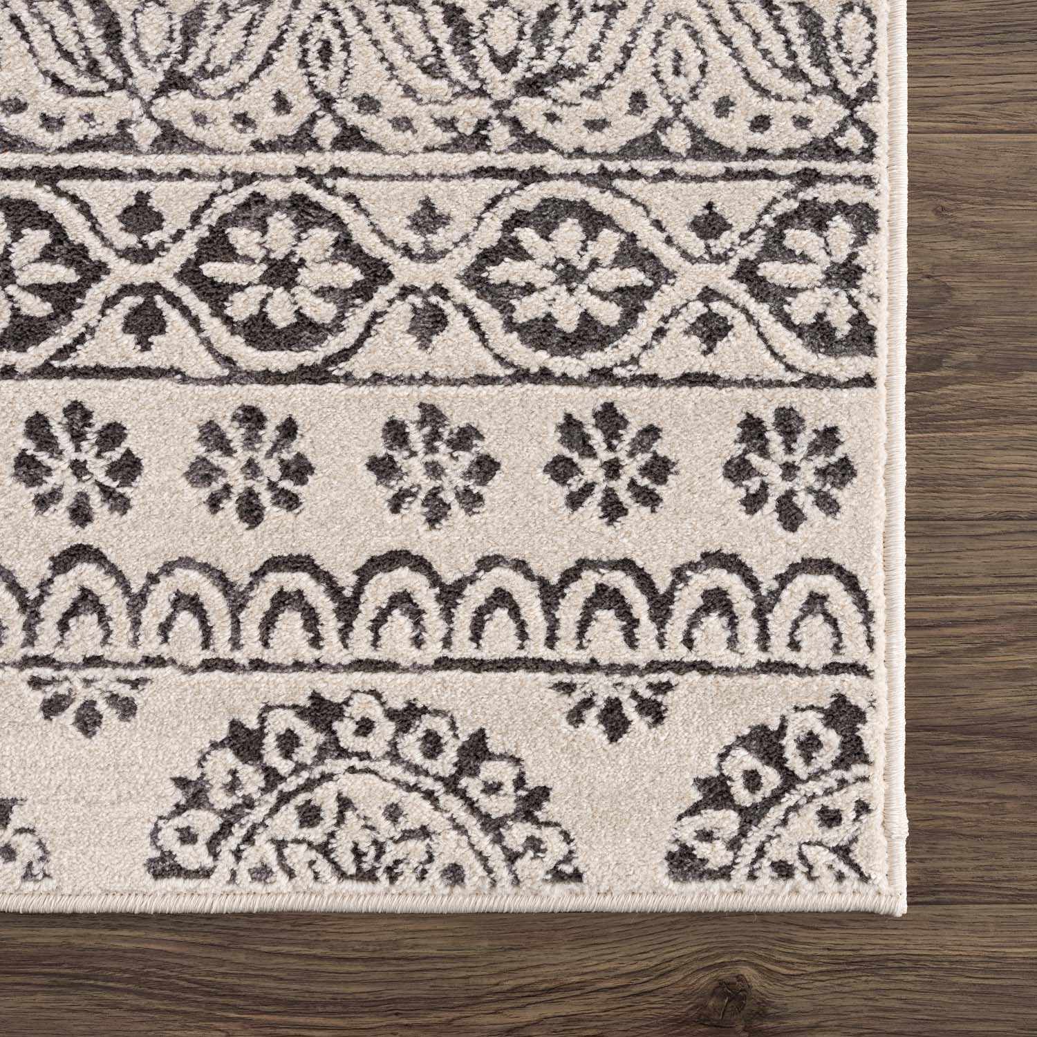 Close-up of the Warroad Area Rug. Charcoal and beige rug with a traditional, floral-inspired pattern. Swatch