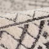 Close-up of the Merriott Area Rug showing its light beige pile and charcoal geometric pattern. Soft texture. Fold