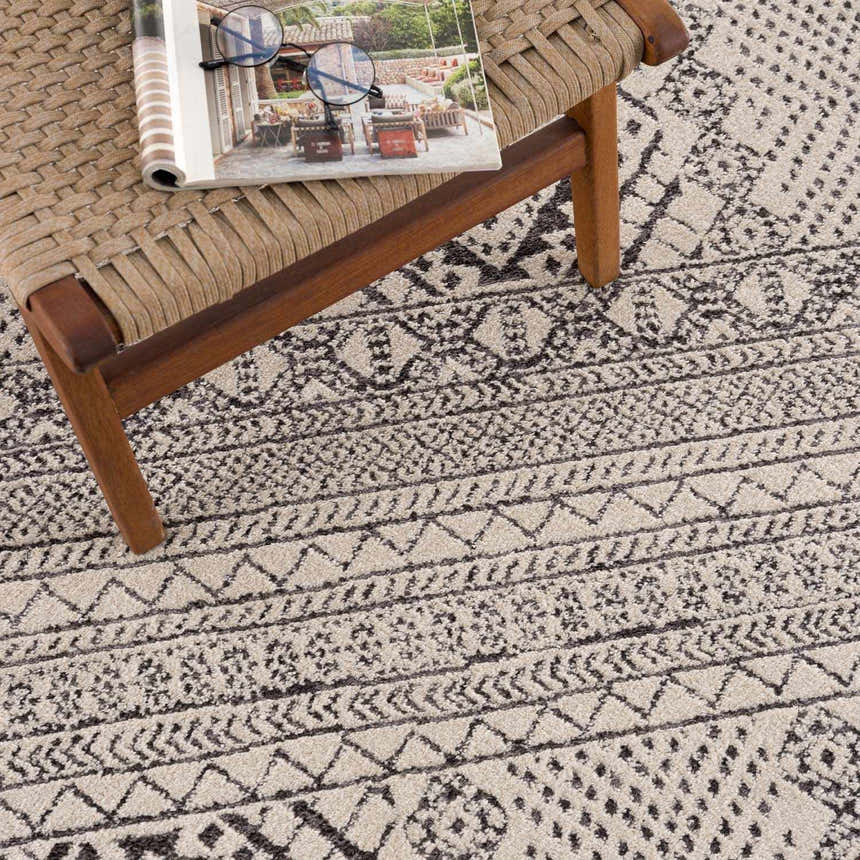 Close-up of the Merriott Area Rug showing its beige base and charcoal, dark brown, geometric, bohemian pattern. Styleshot
