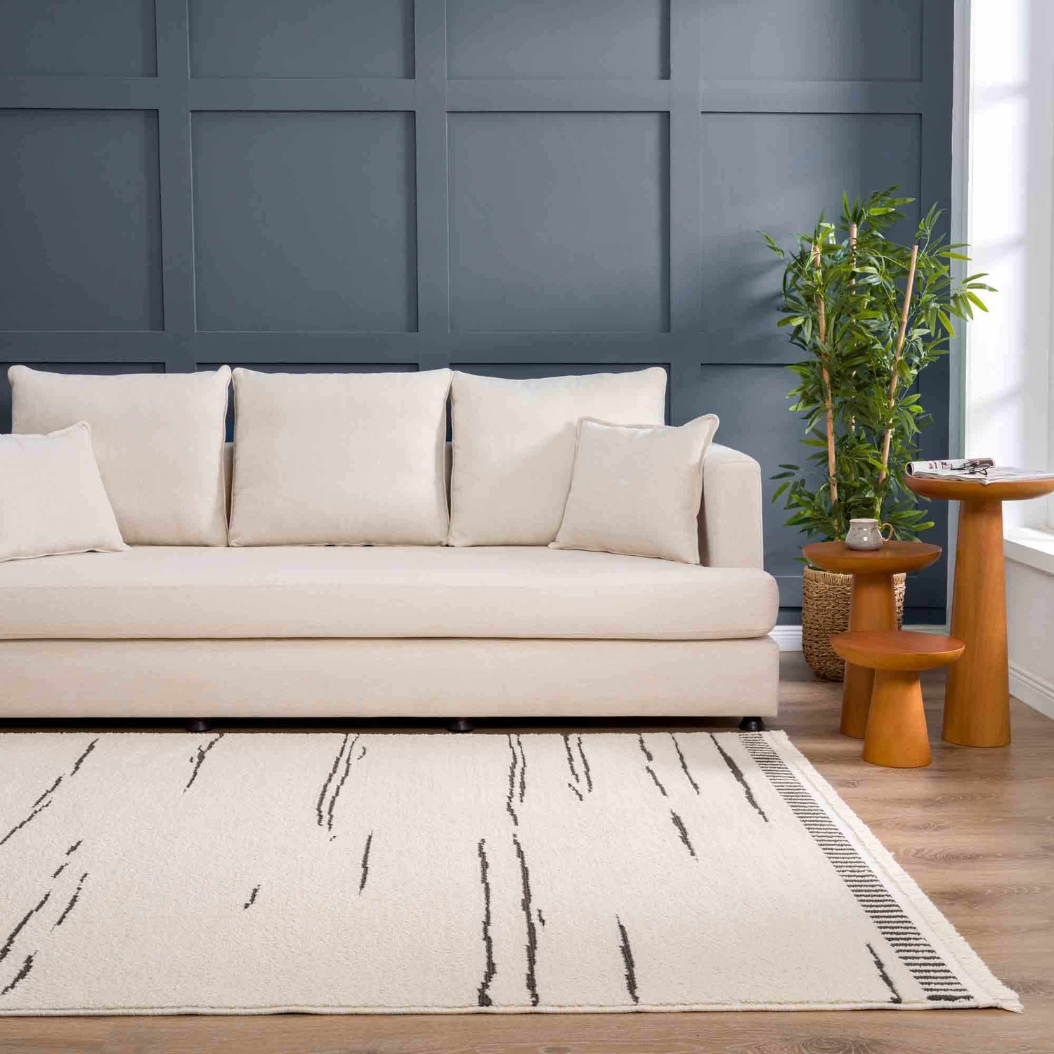 Living room scene with a bone Aulii Area Rug, cream sofa, wood side tables, and blue accent wall. Roomscene-Rectangle