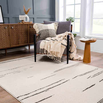 Living room scene with bone Aulii Area Rug, gray chair, wood cabinet, and neutral decor. Roomscene-Rectangle