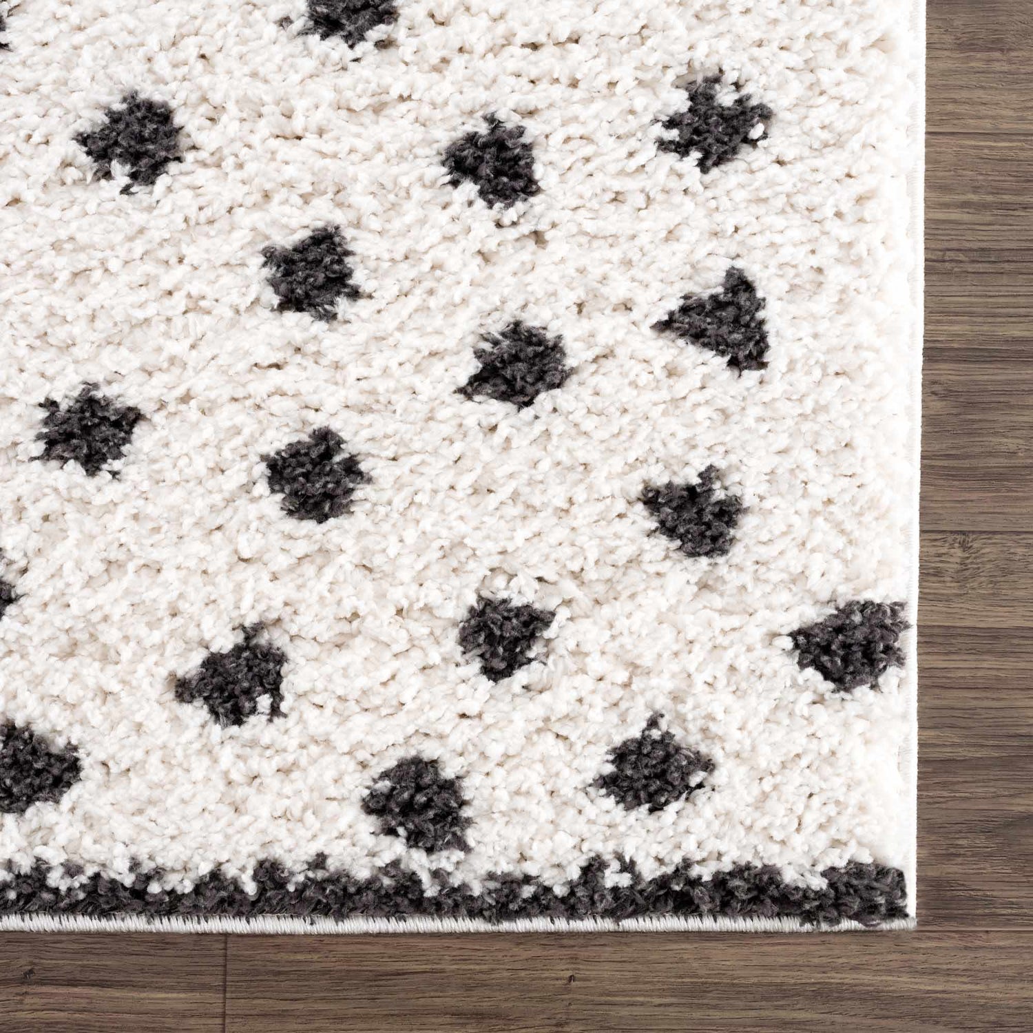 Close-up of the plush Chaia Dotted Black & White Rug showing its soft texture and dotted pattern on a wood floor. Swatch