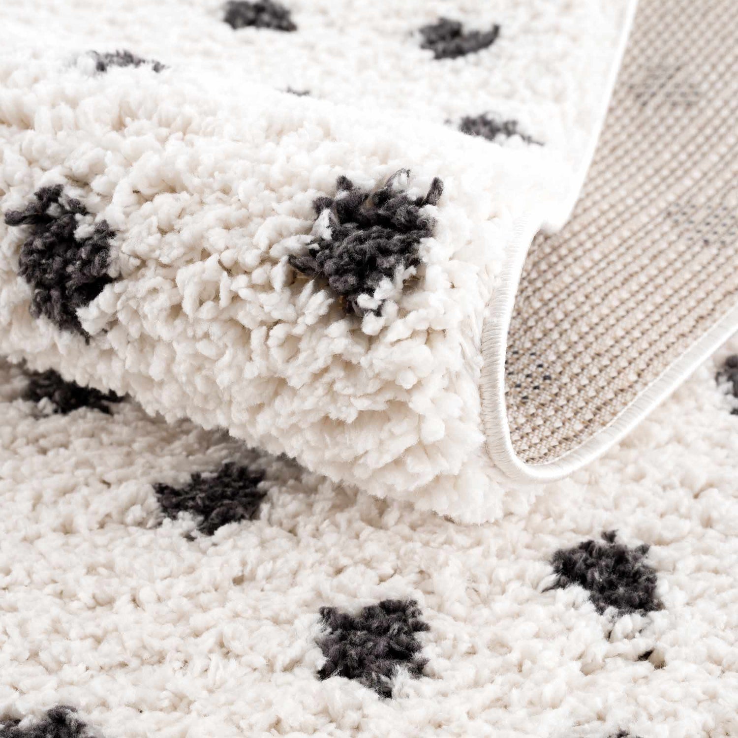Close-up of the plush Chaia Dotted Black & White Rug, showing its soft texture, black dots, and machine-woven backing. Fold