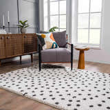 Living room scene with a Chaia Dotted Black & White Plush Rug, gray chair, wood cabinet, and natural light. Roomscene-Rectangle