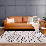 Living room scene with a tan leather sofa and the Chaia Dotted Black & White Plush Rug on a wood floor. Gray accent wall. Roomscene-Rectangle