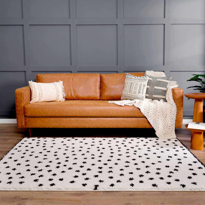 Living room scene with a tan leather sofa and the Chaia Dotted Black & White Plush Rug on a wood floor. Gray accent wall. Roomscene-Rectangle